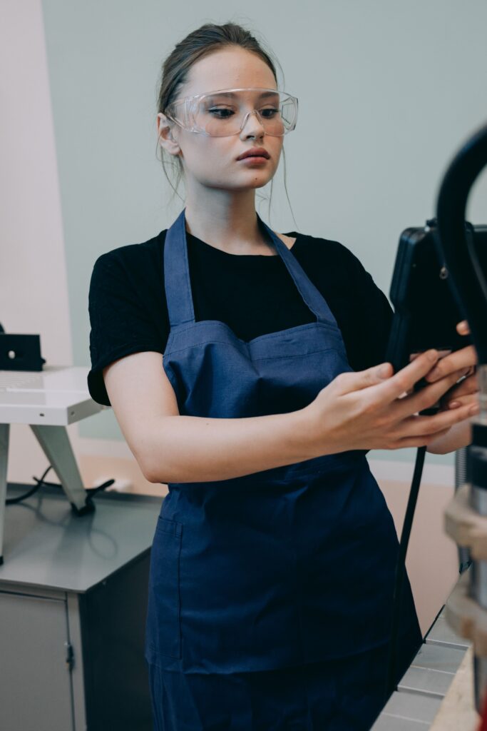 aerospace Young woman in apron and safety goggles operating equipment indoors.